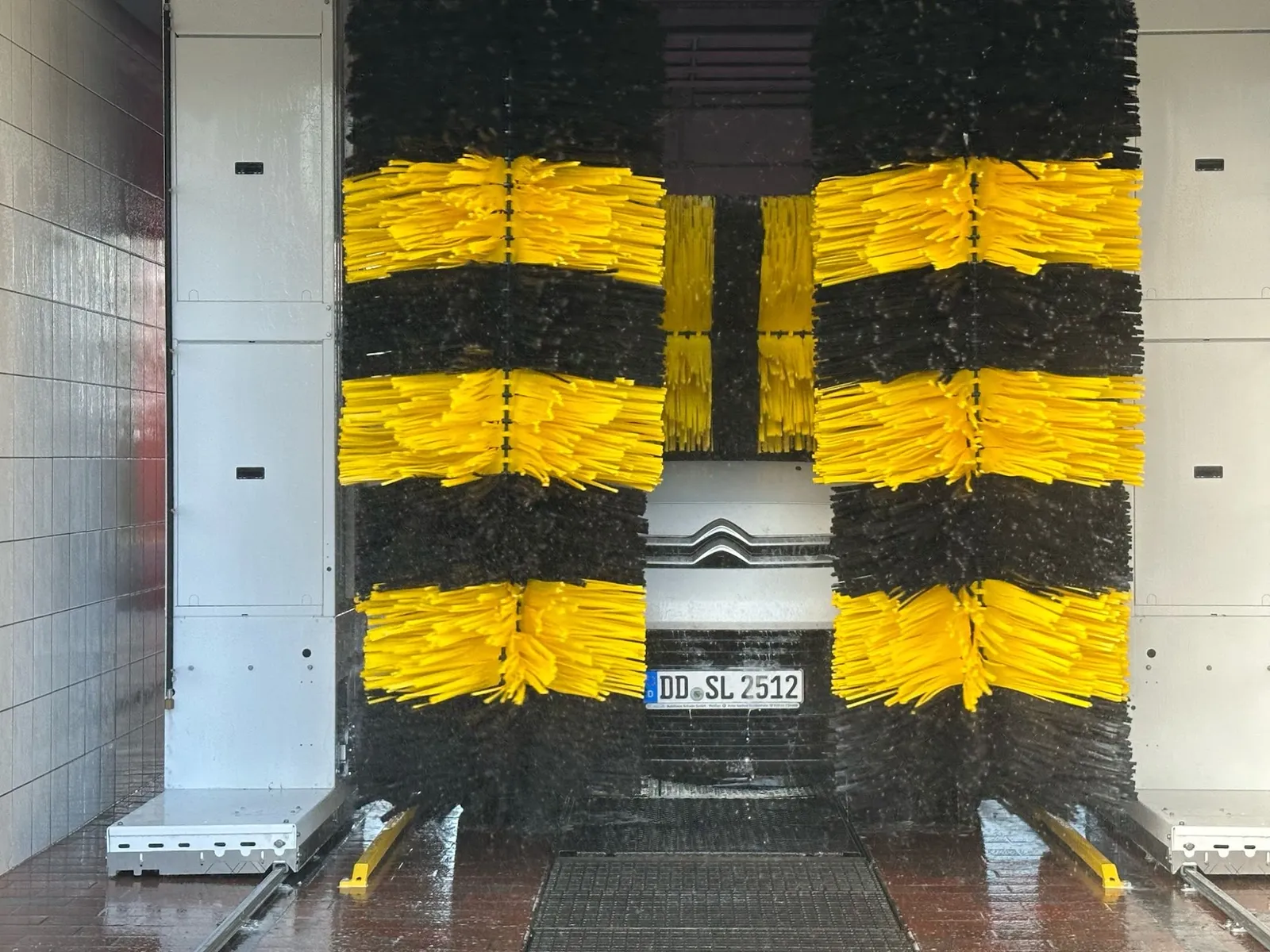 Weißer Lieferwagen umschlossen von gelb-schwarzen Textil-Waschbürsten der Waschanlage